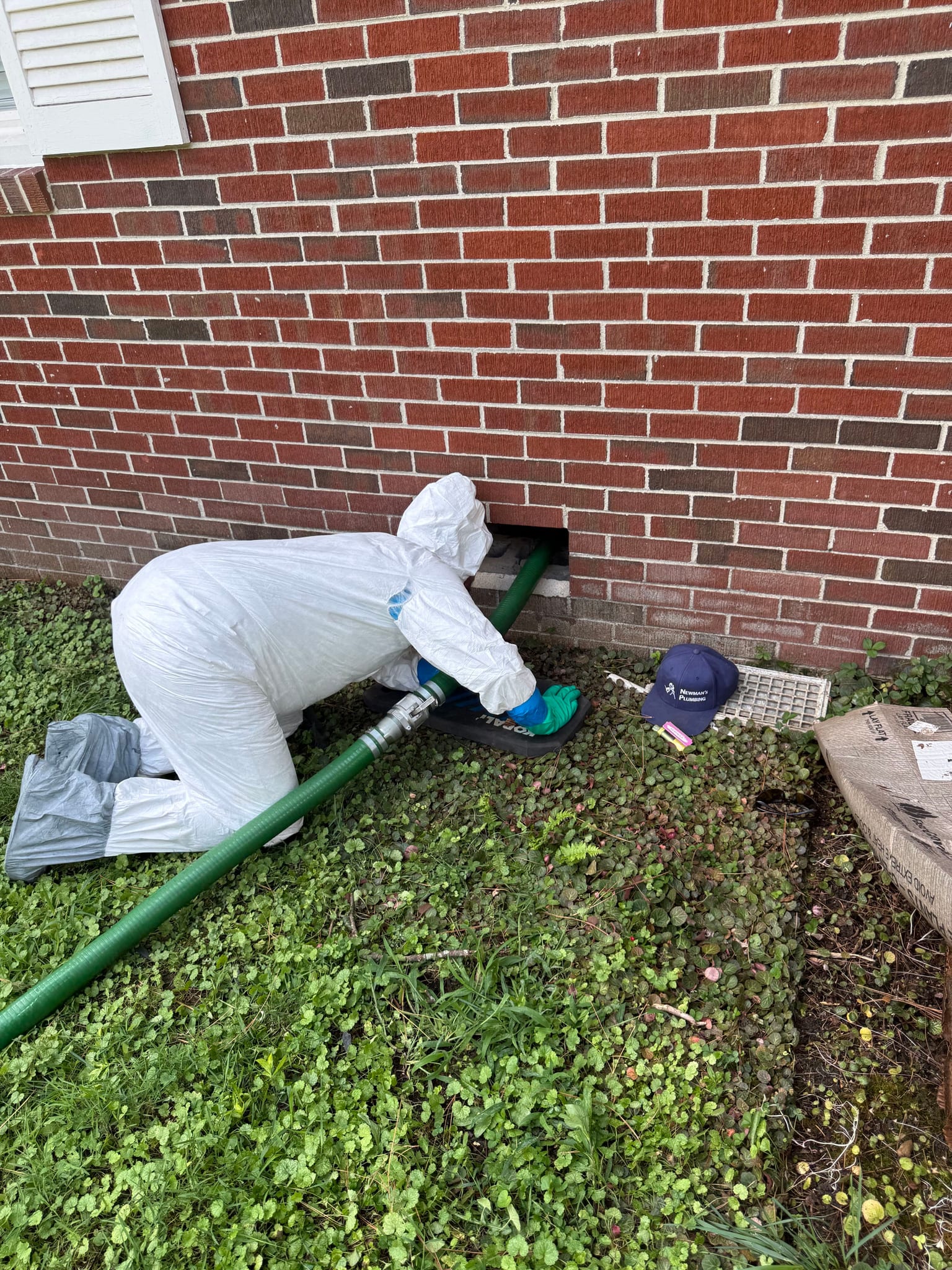 Newman's Plumbing technician in protective coveralls running a suction line into a crawlspace in Portsmouth, VA